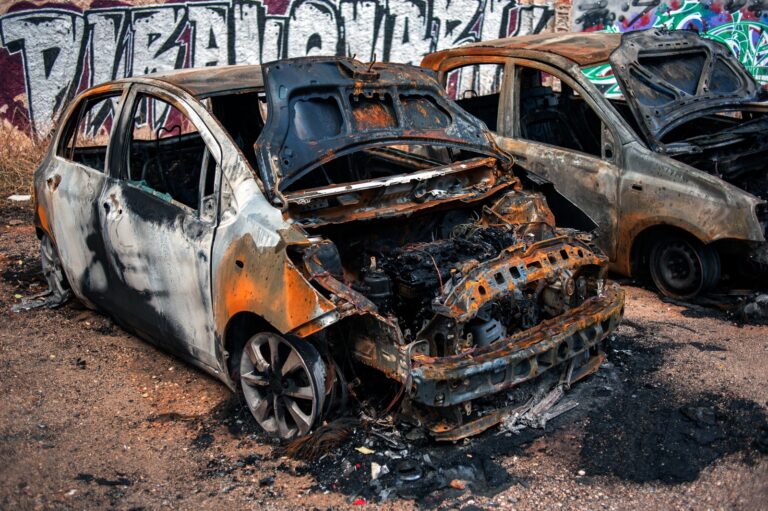 Two cars in a parking lot that have been burnt out.