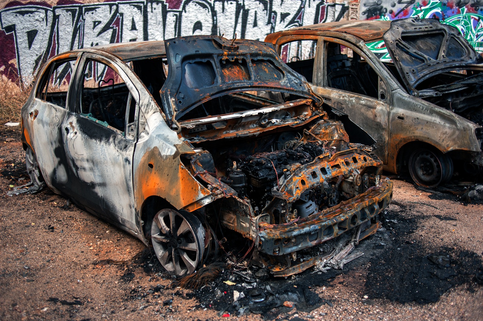 Two cars in a parking lot that have been burnt out.