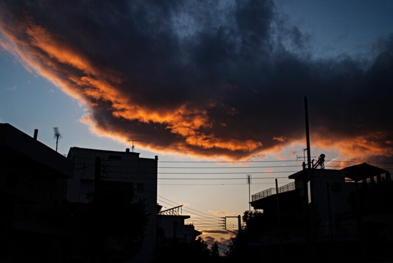 A storm cloud passing over the city with bright orange underside and the buildings in silhouette