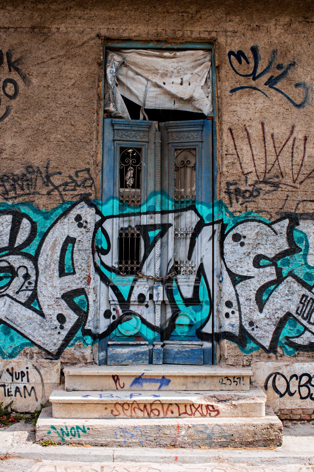 A blue door to an abandoned building covered with graffiti and a large chain on it