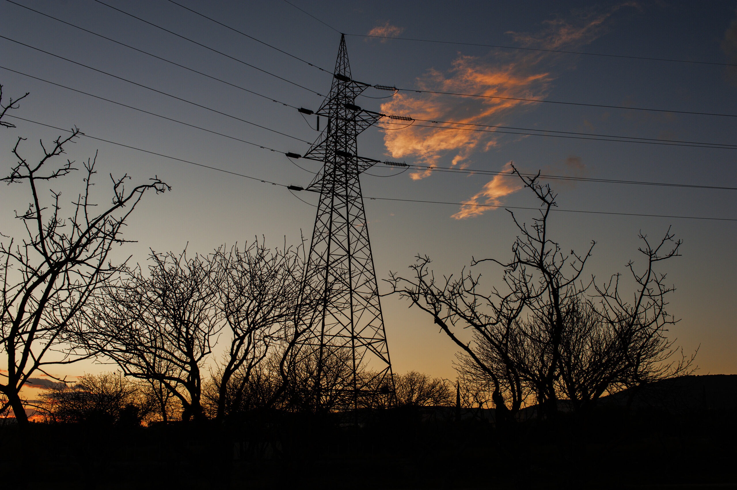 A large electrical pylon in silhouette against a sunset sky in early evening
