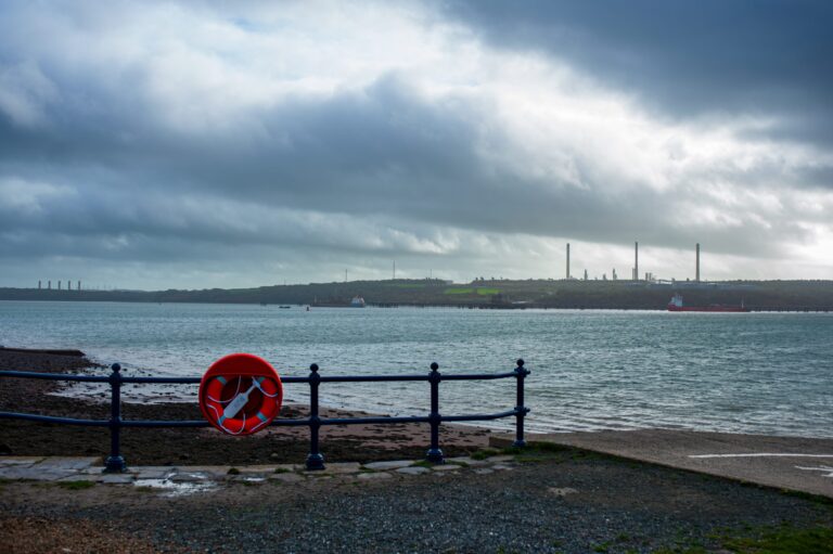 An orange lifebuoy or lifesaver on a fence beside the shore in Milford Haven against a background of a looming storm.