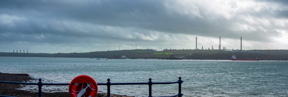 An orange lifebuoy or lifesaver on a fence beside the shore in Milford Haven against a background of a looming storm.