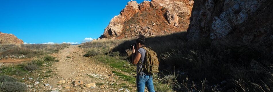A photograph of Cassi Moghan with a camera on a mountainside taking photos of the rocky landscape.