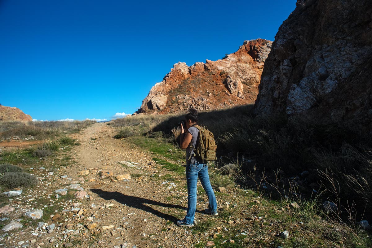 A photograph of Cassi Moghan with a camera on a mountainside taking photos of the rocky landscape.