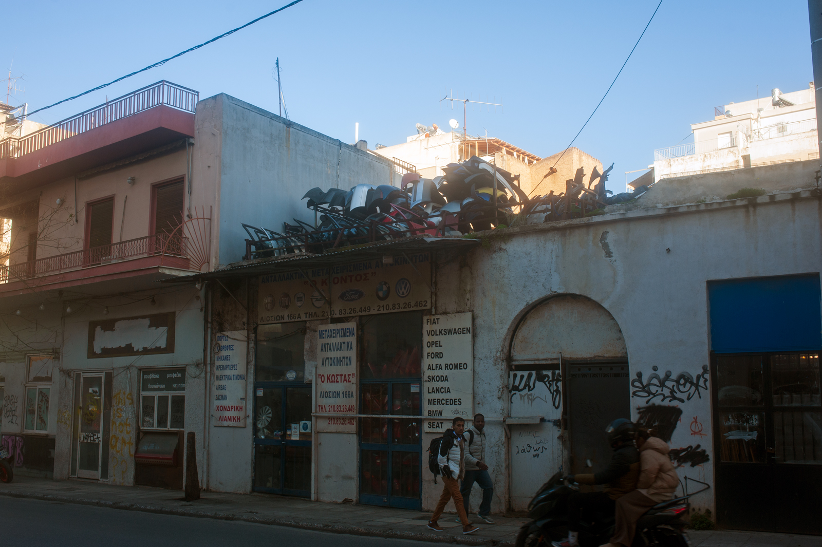 Abandoned shop fronts with a pile of broken cars on the roof.