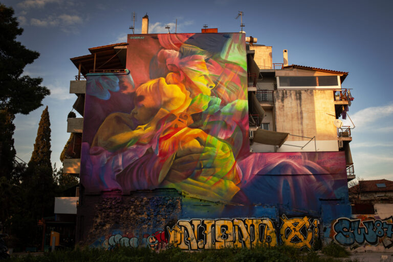 A building in Nea Philadelphia in Athens with a giant mural painted on the side. Photographed during golden hour.