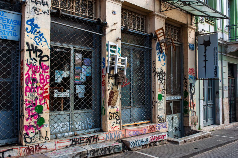 A photograph of an abandoned shop in downtown Athens with two chairs hanging on the outside wall.
