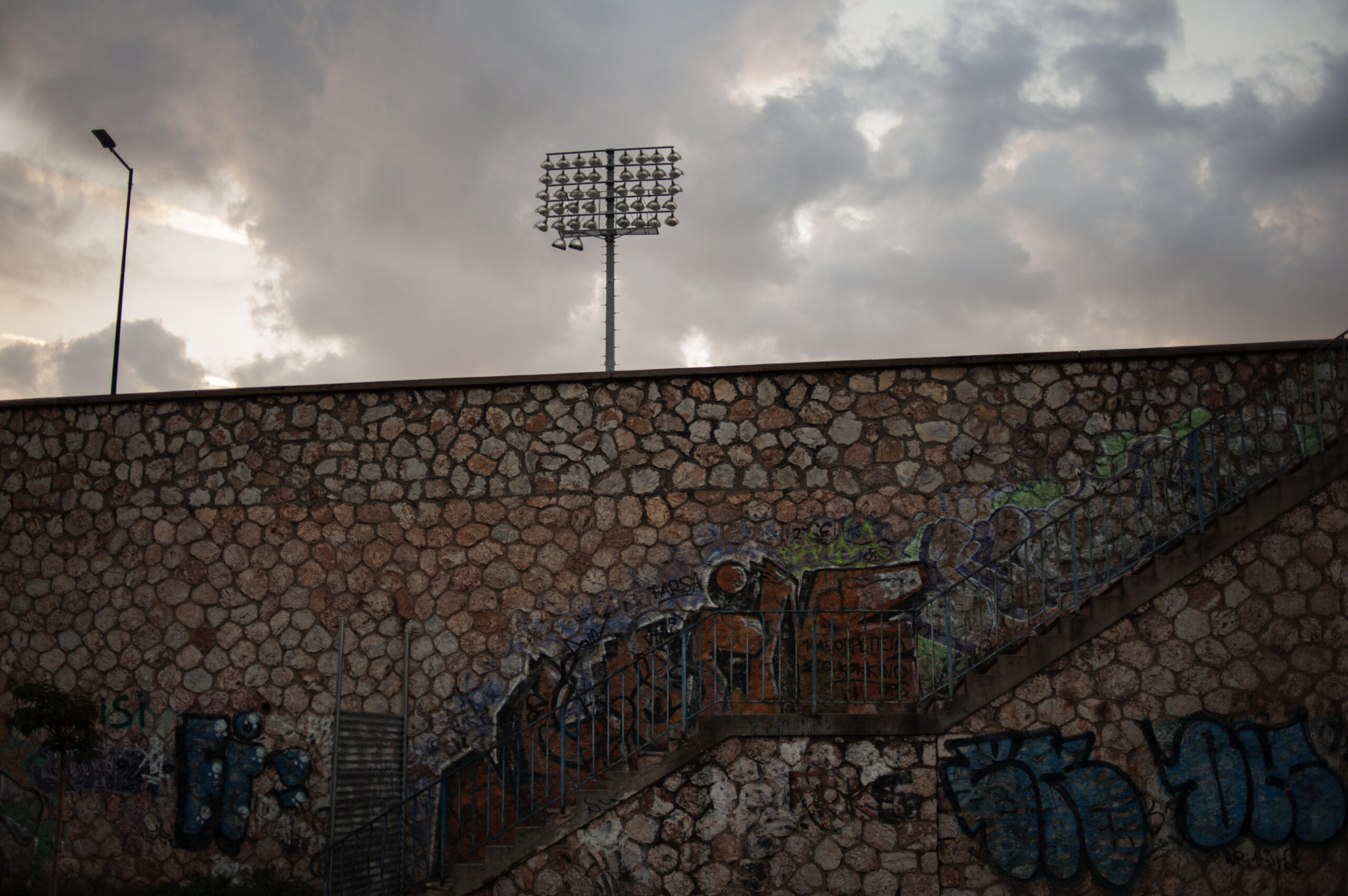 A colour photograph looking over the wall of an old football stadium in the early evening. Strong clouds in the background.