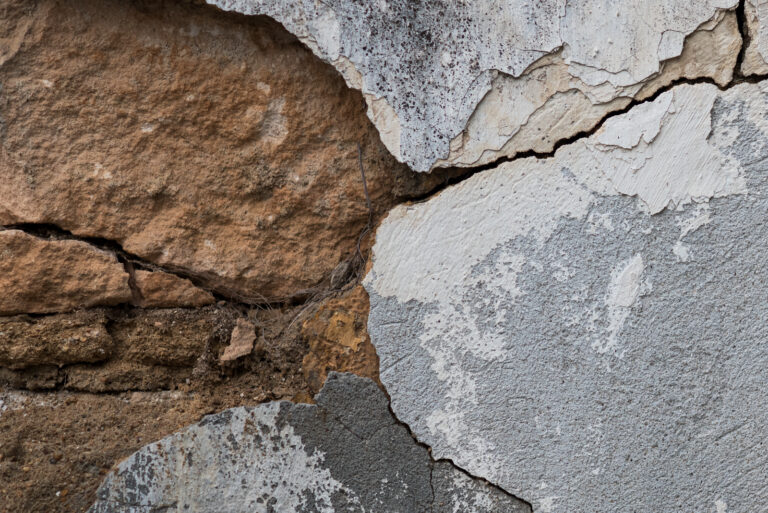 A closeup of a cracked wall with concrete and stone showing underneath.