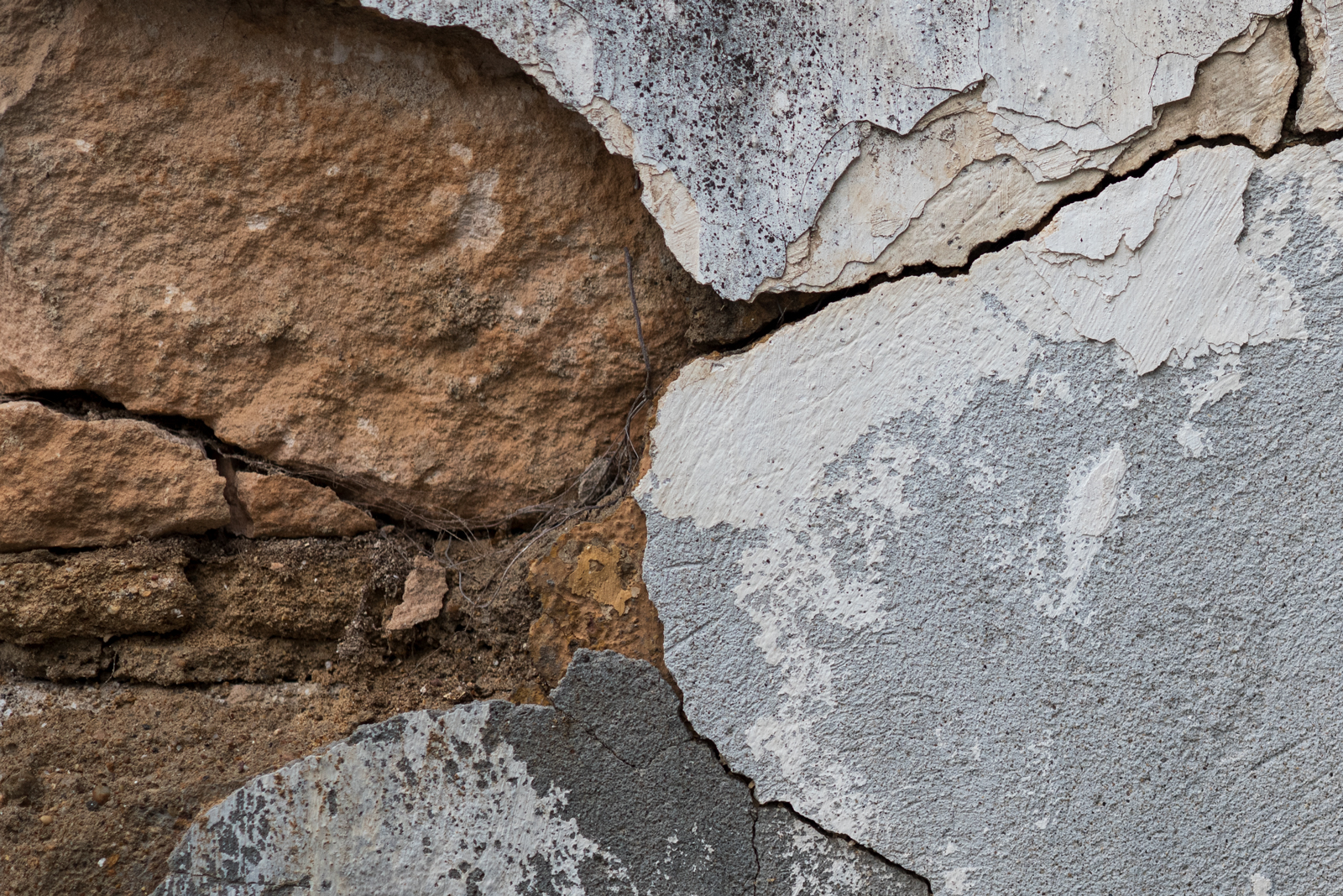 A closeup of a cracked wall with concrete and stone showing underneath.